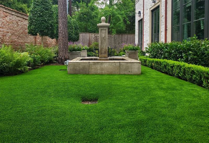 Backyard landscape design featuring a decorative fountain and a grass lawn in Houston, TX