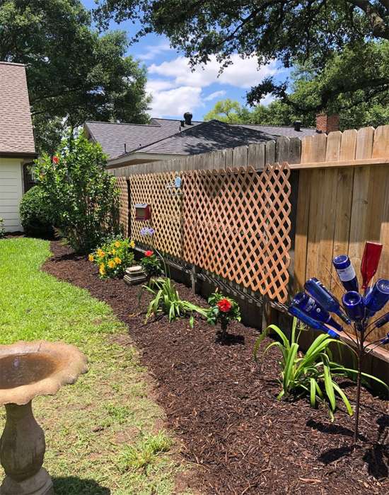 Landscaped garden bed with fresh mulch and plants, and decorative bottle art in Houston, TX