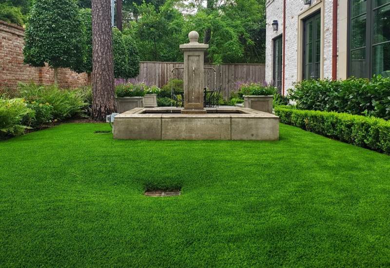 A neatly mowed green lawn with a central stone fountain in Houston, TX