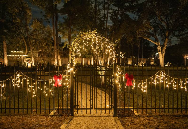 Christmas light decorations draped over a garden gate with warm string lights in Houston, TX