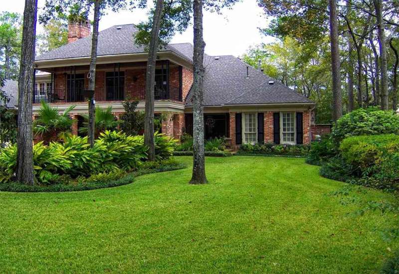 Lawn care services featuring a neatly mowed green yard around a brick house in Houston, TX