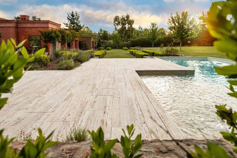 Stone patio with modern pool, manicured lawn, and landscaped garden setting, in Houston, TX
