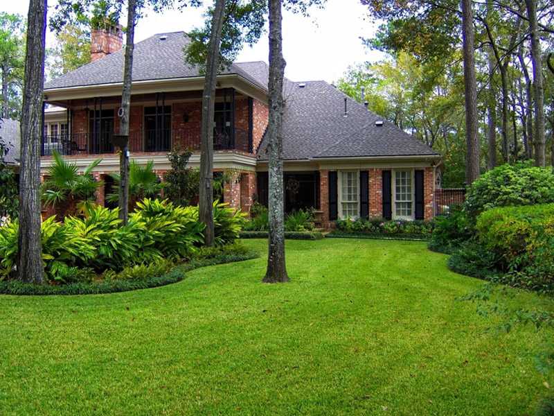 Brick home with manicured lawn, mature trees, and landscaped garden beds, in Houston, TX
