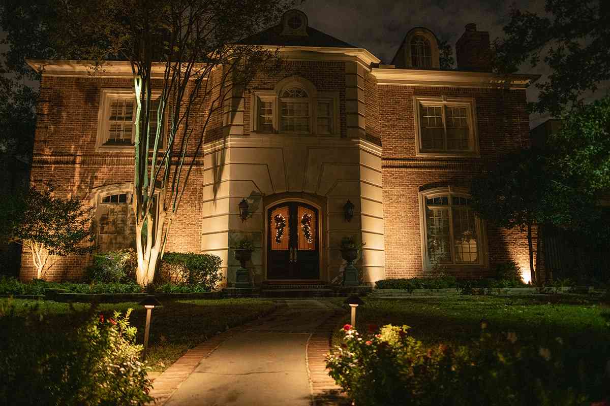 Brick home with professional landscape lighting, illuminated trees, and walkway, in Houston, TX