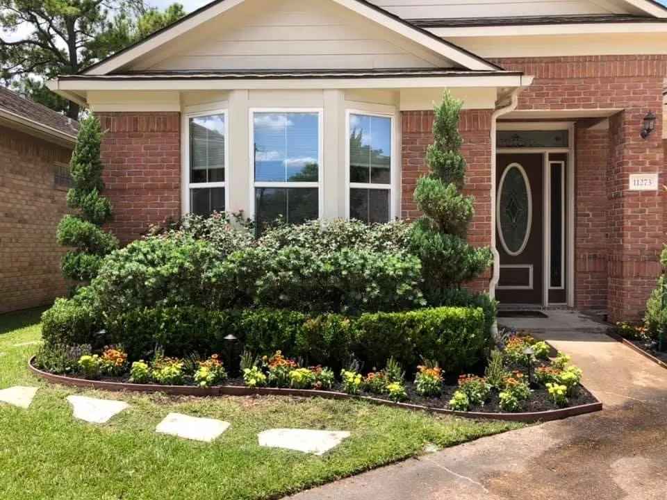Brick home with manicured lawn, trimmed shrubs, and colorful flower beds, in Houston, TX
